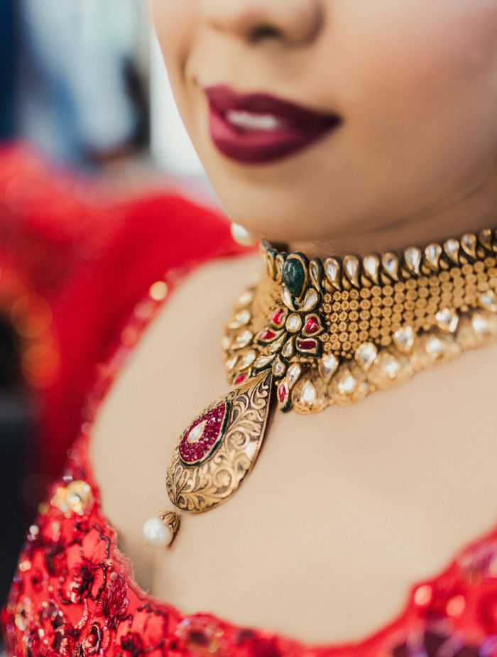 Home Close-up of elegant bridal jewelry worn by a woman in vibrant red attire, showcasing intricate designs.