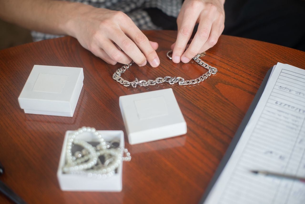 Home Hands arranging a silver chain necklace on a wooden table with jewelry boxes, indoors.