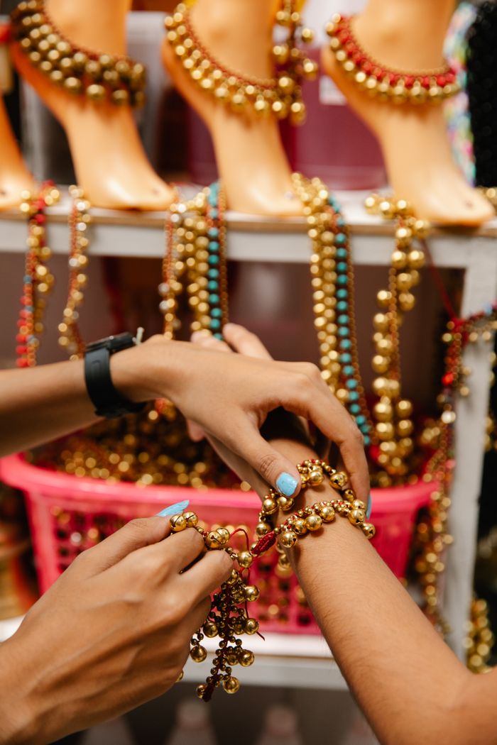 Home Hands trying on vibrant beaded jewelry at an indoor market stall.